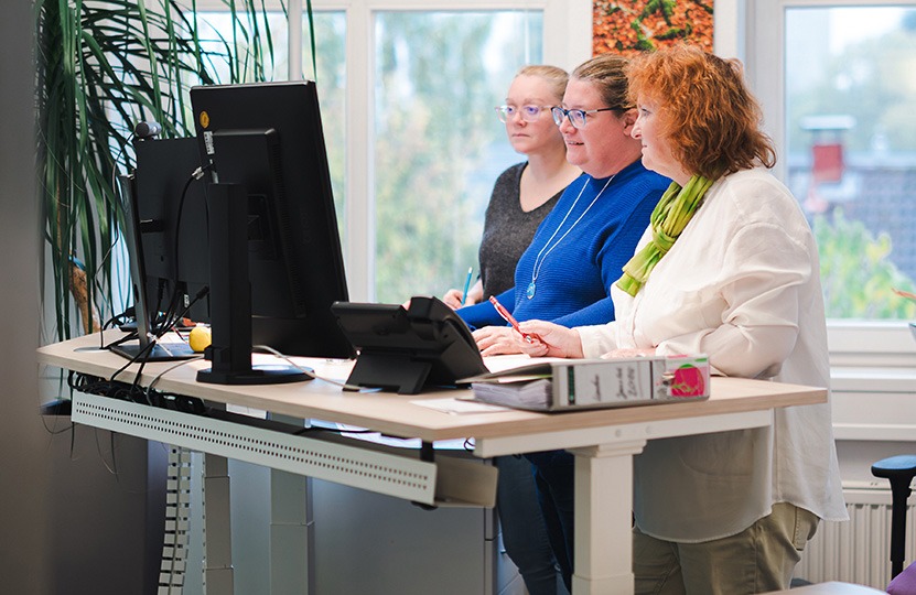 drei Kolleginnen der Kanzlei stehen und arbeiten gemeinsam an einem Schreibtisch